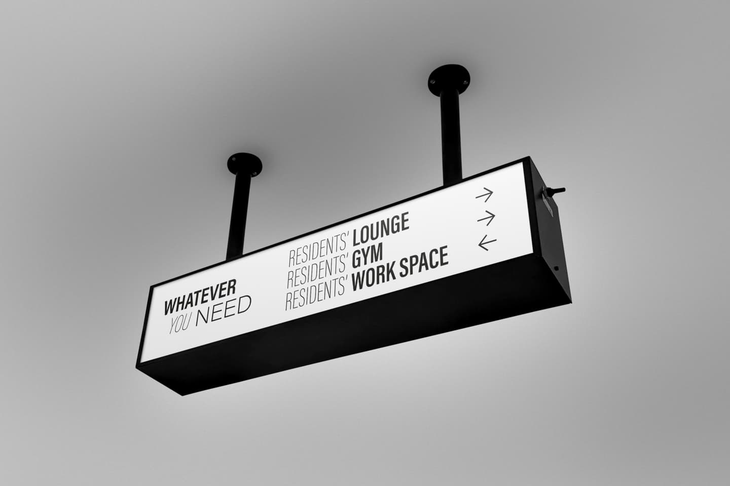 Rectangular ceiling sign with black text and arrows directing to residents' lounge, gym, and workspace. The words Whatever you need are displayed on the left.