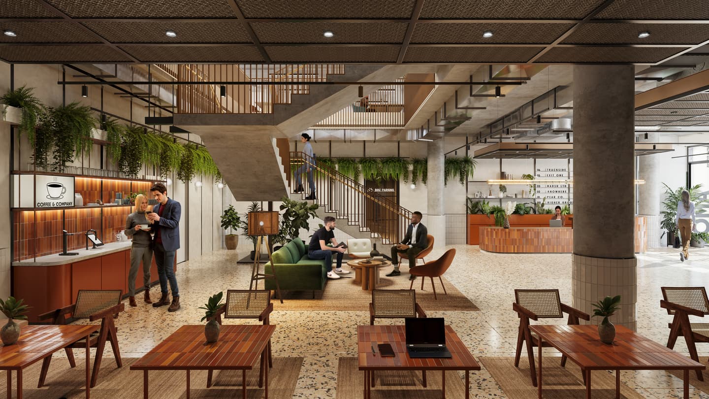 Modern coworking space with open seating, indoor plants, a coffee lounge, people working and conversing, and a central staircase leading to an upper floor.