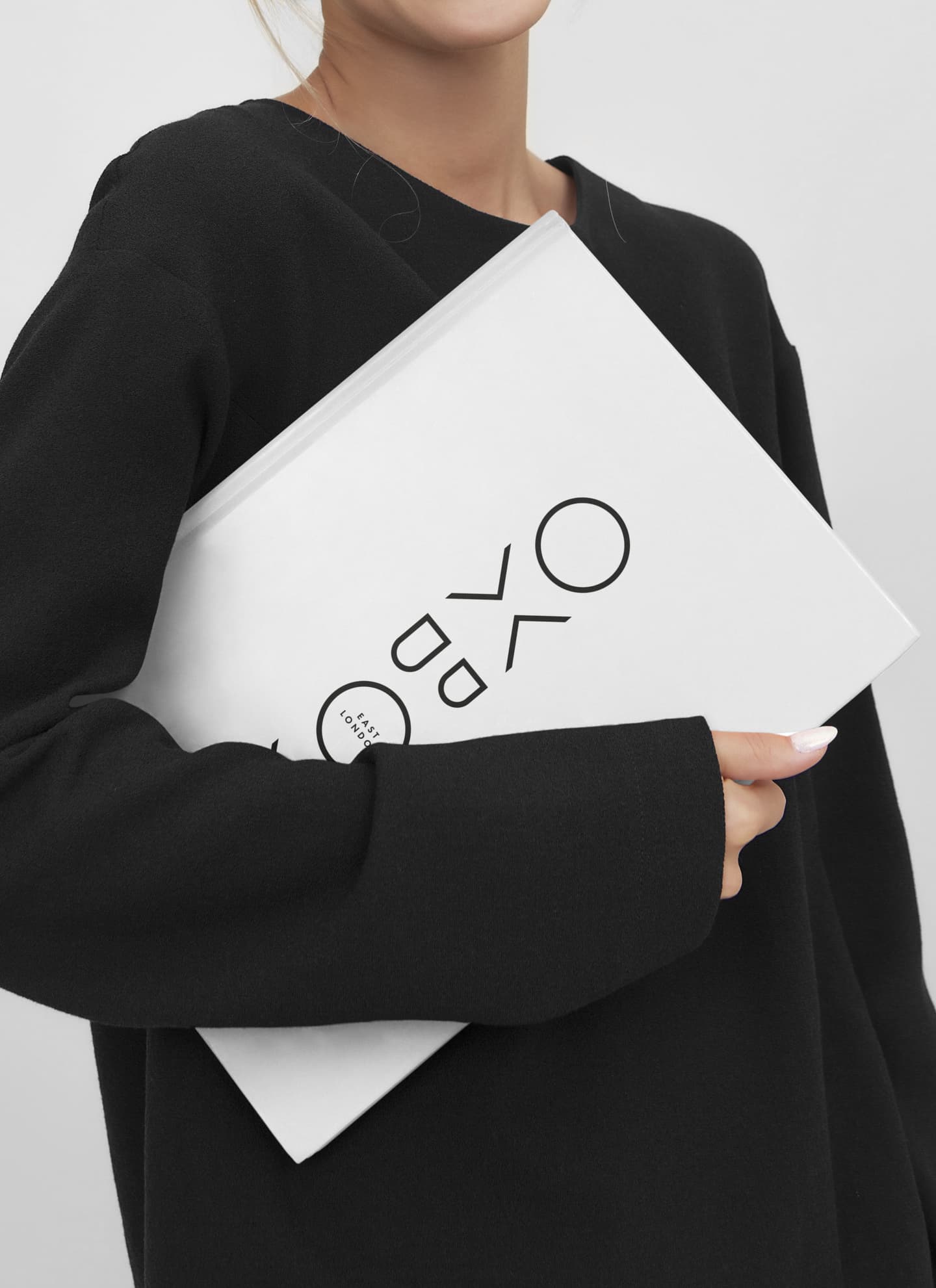 A person in a black top holds a large white book with abstract black lettering on the cover, against a plain background.