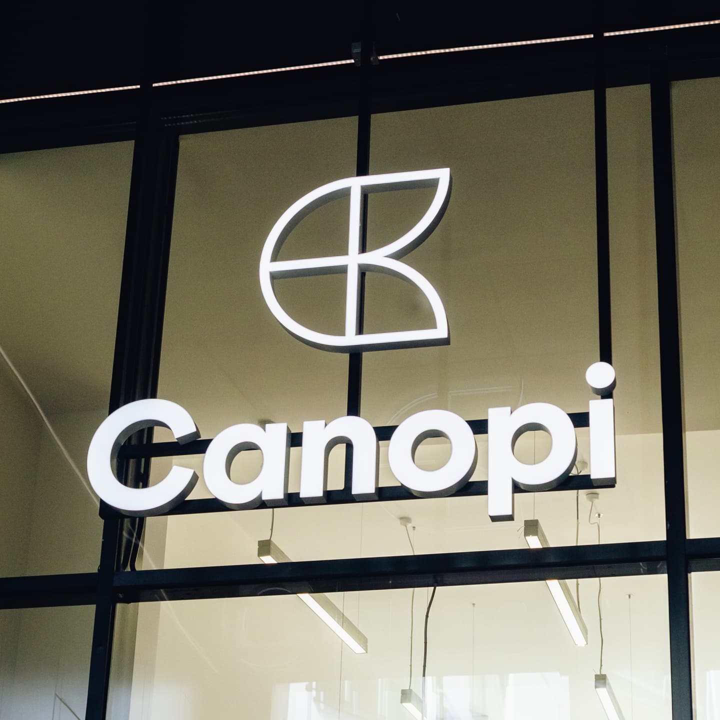 Illuminated Canopi sign with a geometric leaf logo above it, mounted on a glass building façade.