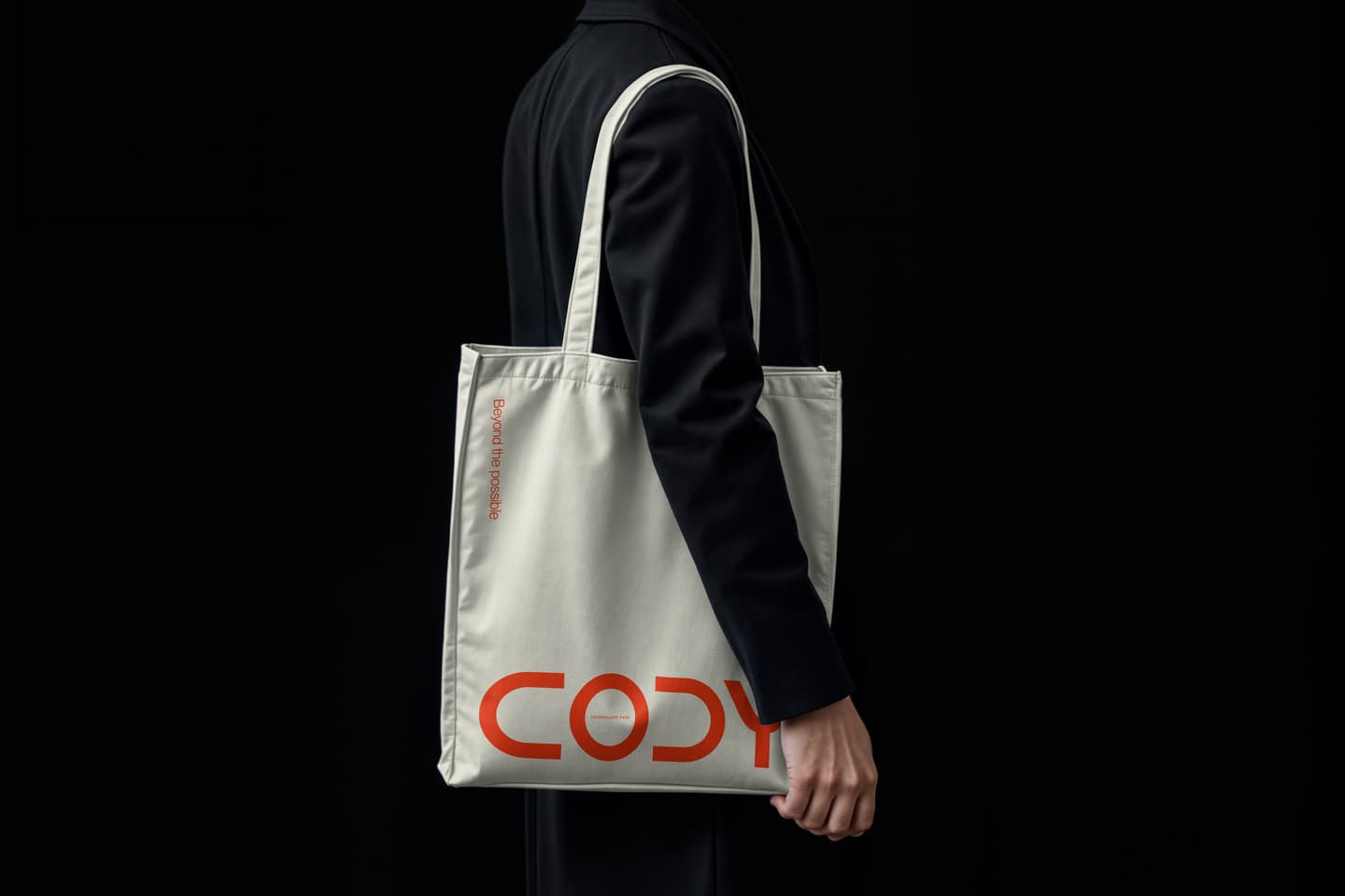 A person in a black outfit holds a white tote bag with the word CODY and small red text printed on it, against a black background.