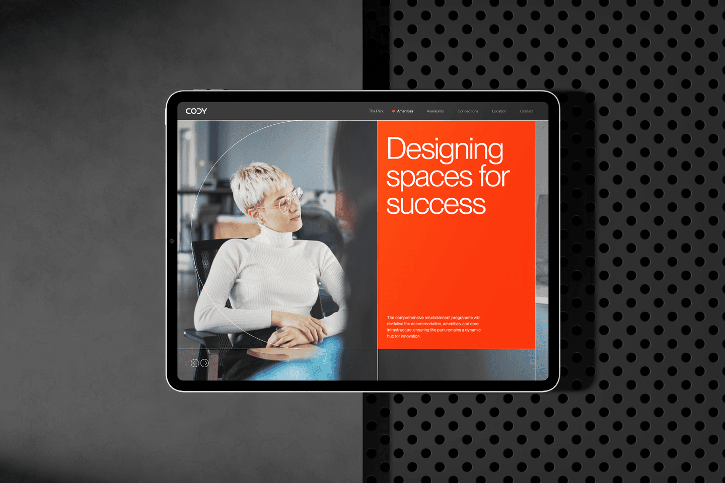 A tablet displays a website with a photo of a person in glasses and white polo-neck, next to large orange text reading Designing spaces for success.